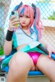 A woman with pink hair sitting on a bench holding a cell phone.