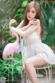 A woman in a white dress sitting on a white chair next to a pink flamingo.