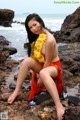 A woman sitting on a rock by the ocean.