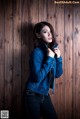 A woman in a denim jacket leaning against a wooden wall.