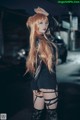 A woman with long red hair standing on a street at night.