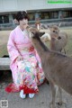 A woman in a kimono feeding a deer with a cup.