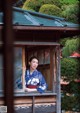 A woman in a blue kimono looking out of a window.