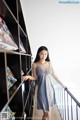 A woman in a blue dress standing next to a bookshelf.